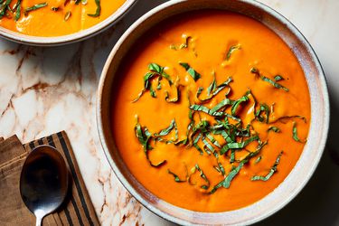 Overhead view of two bowls of tomato soup with shredded greens on top