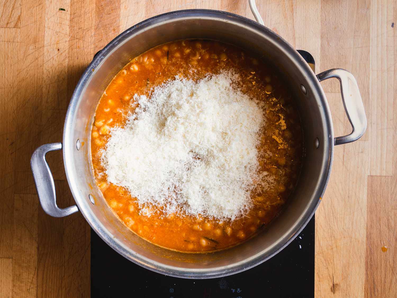 An overhead of grated cheese on top of the pasta e ceci in the pot it was cooked in.