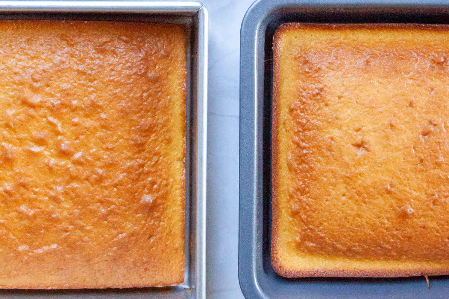 Two square baking pans with baked cakes in them.