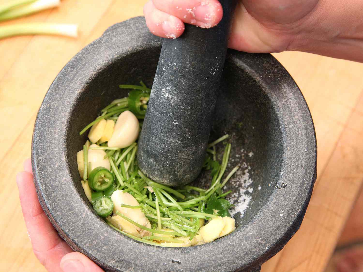 Pounding garlic, ginger, thick cilantro stems, and chile with a mortar and pestle. 