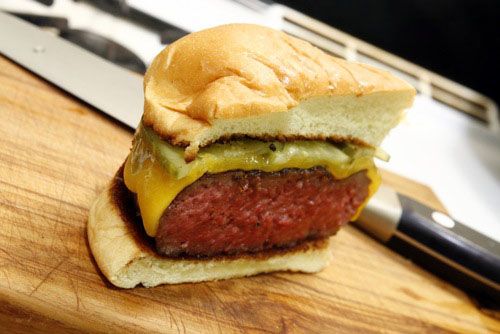 A cheeseburger on a bun, cut in half, showing how the interior of the burger is very pink and almost uncooked.