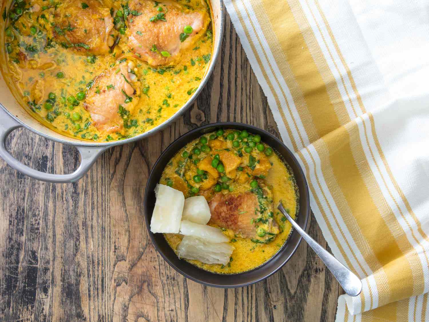 Overhead shot of a pot of chicken braised in coconut milk and ají amarillo pepper paste, served up in a bowl with spoon.