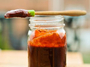 A mason jar filled with homemade cherry barbecue sauce, and a silicone pastry brush dipped in sauce is laying across the rim of the jar.
