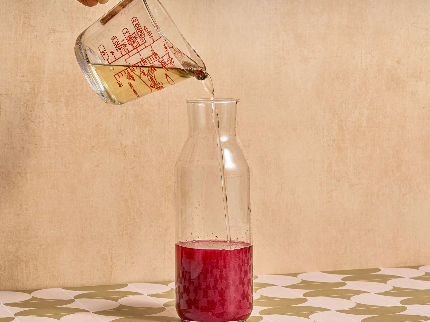 Pouring clear liquid into a carafe containing red liquid