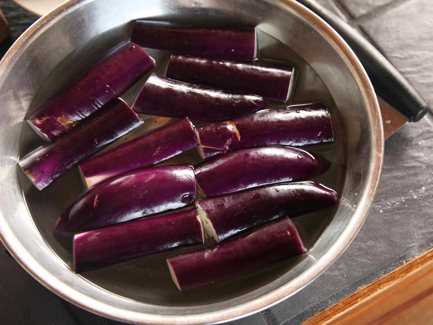 Eggplant pieces soaking in a salt water brine. 