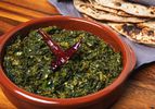 Saag in an earth-toned orange bowl with roti in the background
