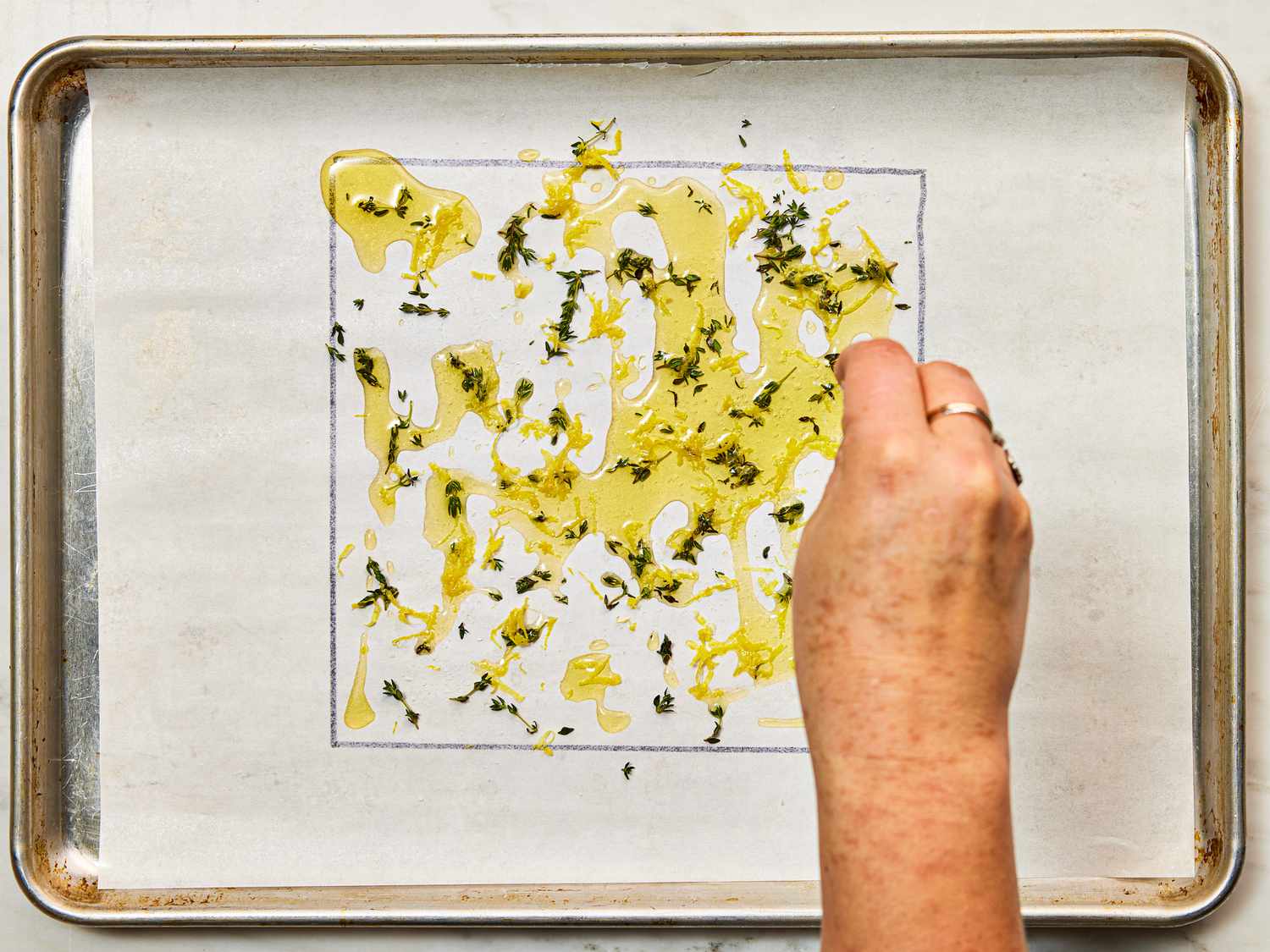 Overhead view of sprinkling herbs on parchment paper