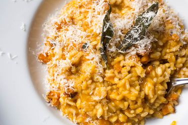 A close-up overhead view of butternut squash risotto made in a pressure cooker, topped with cheese and sage leaves.
