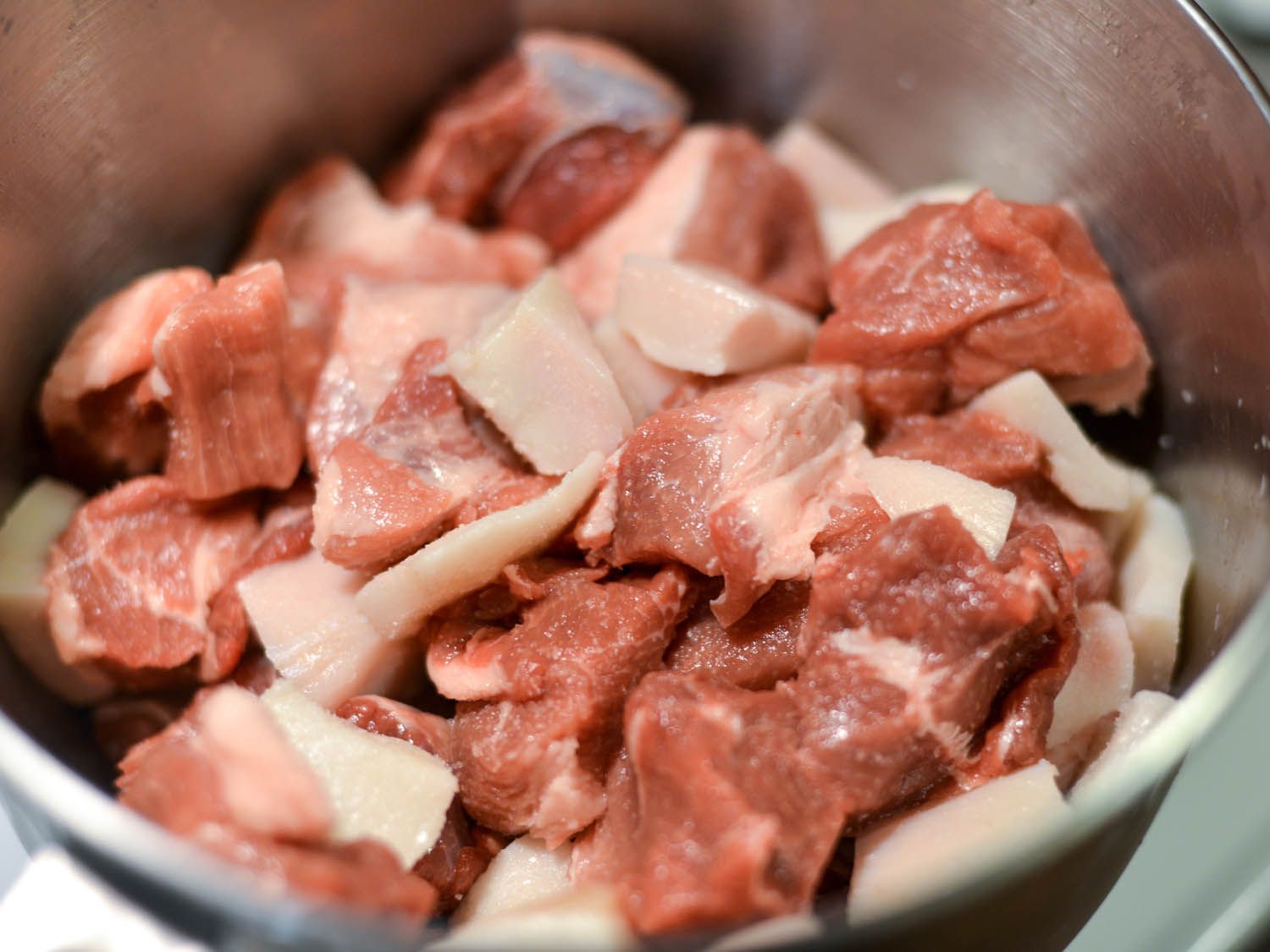 Chilled chunks of lamb, pork, and fatback are combined in a mixing bowl.