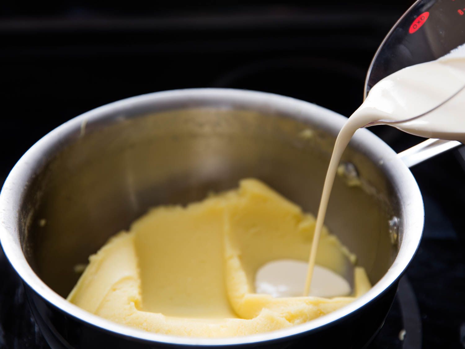 Cream being poured into a pot of mashed potatoes
