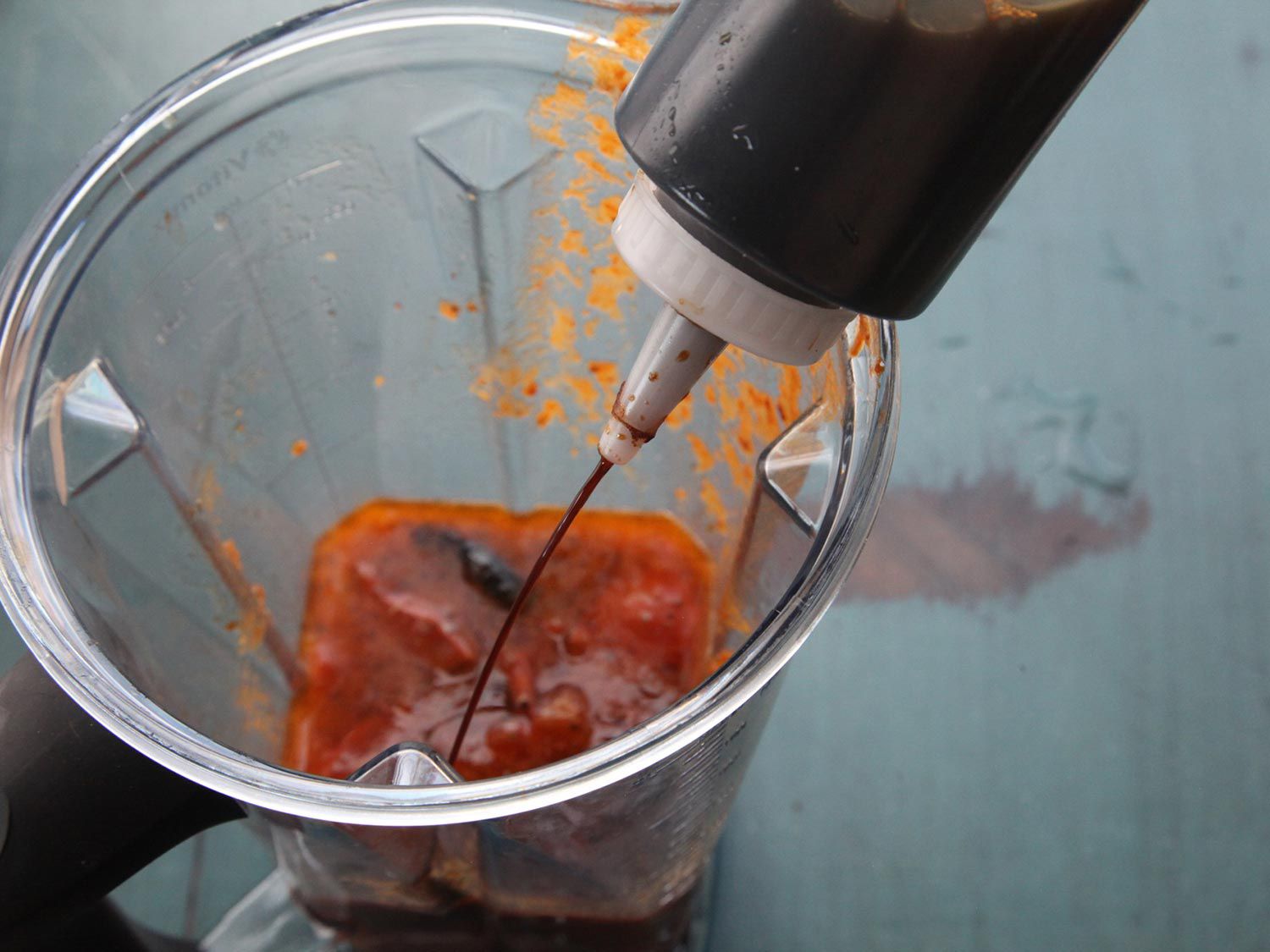 Adding soy sauce to a blender containing the pureed sauce. 