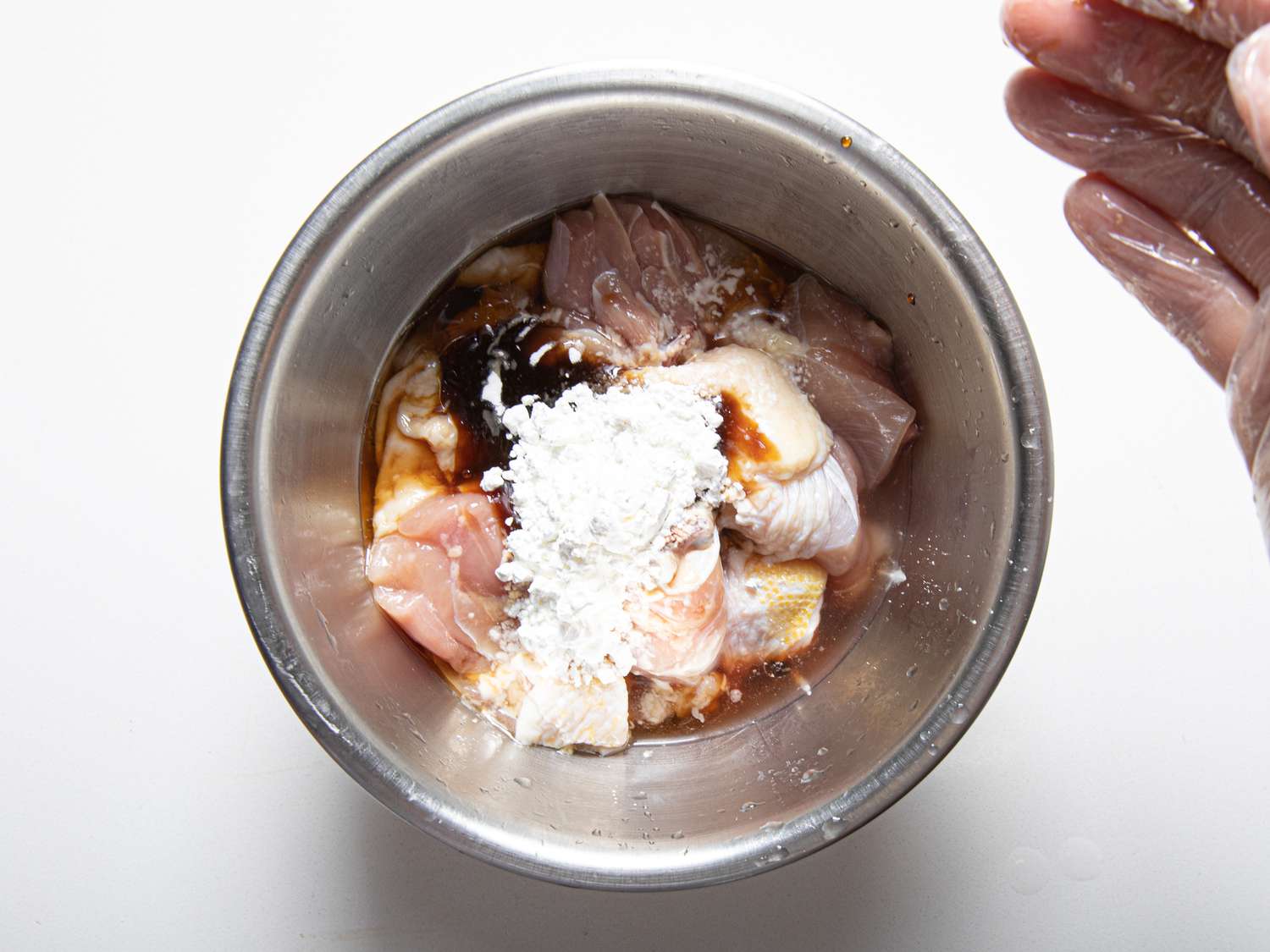 Cornstarch being added to raw chicken.