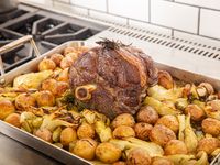 A cooked roast sitting atop browned potatoes and fennel in a roasting pan