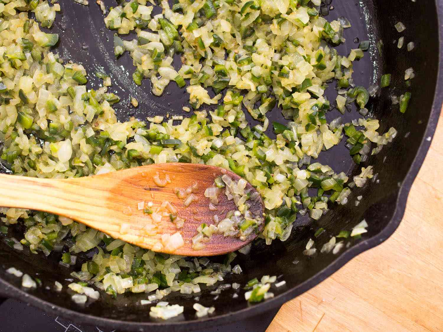 Stirring small-diced onions and chiles in a cast iron skillet and stirring with a wooden spoon.