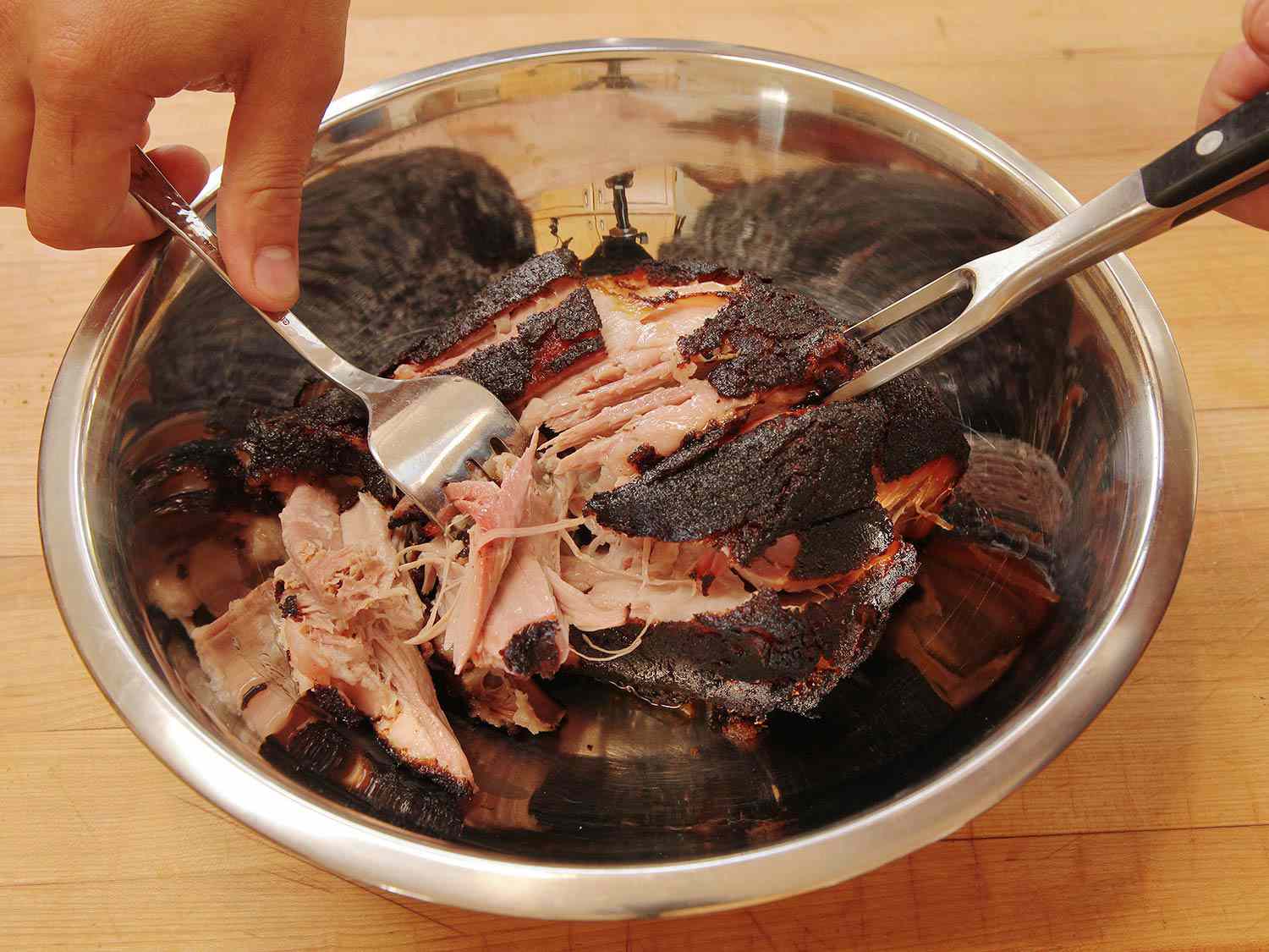 shredding cooked pork shoulder in a bowl with two forks. 
