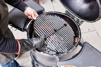A person places a metal grill into the Broil King Keg Kamado Charcoal Grill