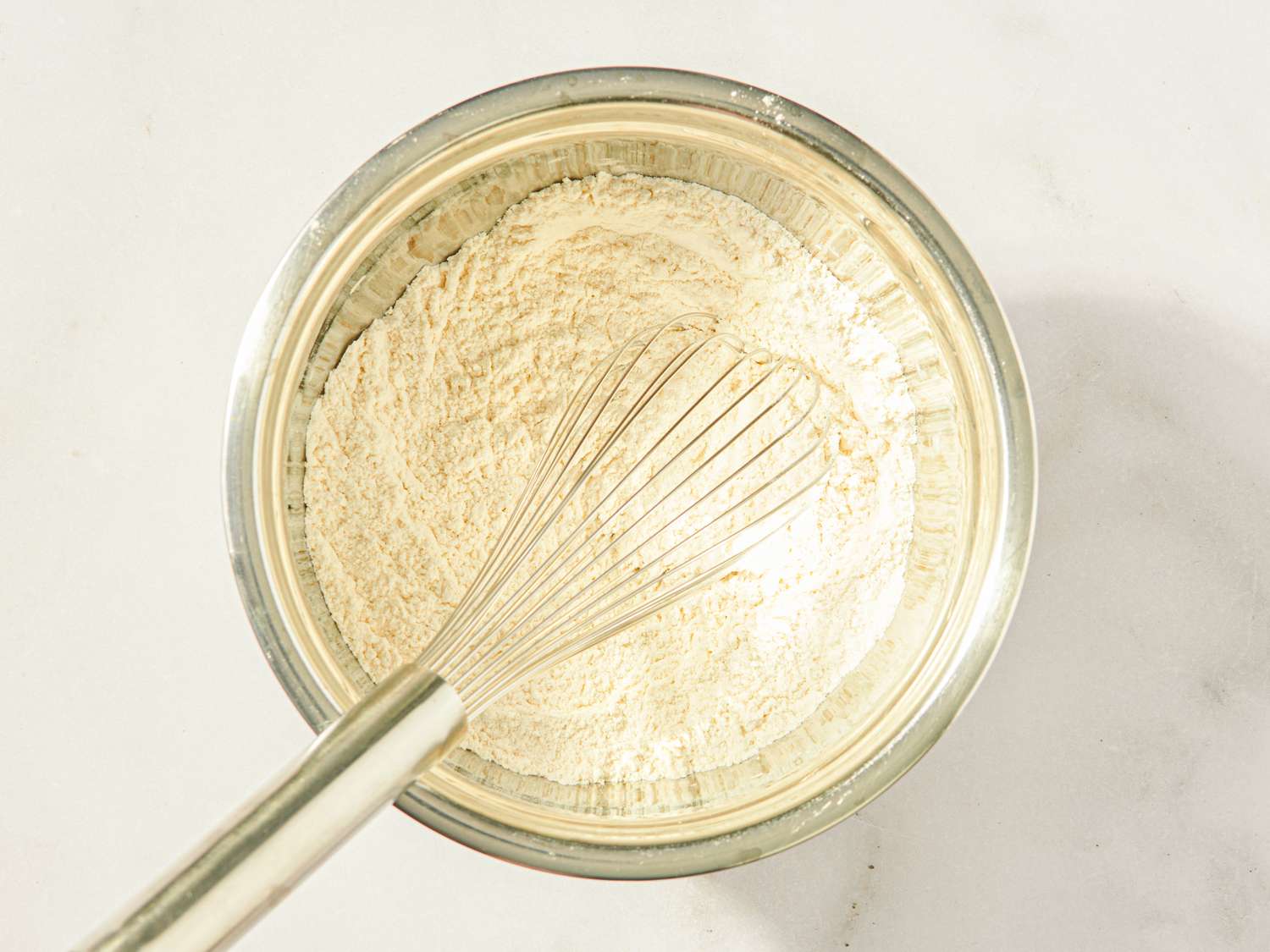 A metal bowl containing dry ingredients being whisked with a metal whisk