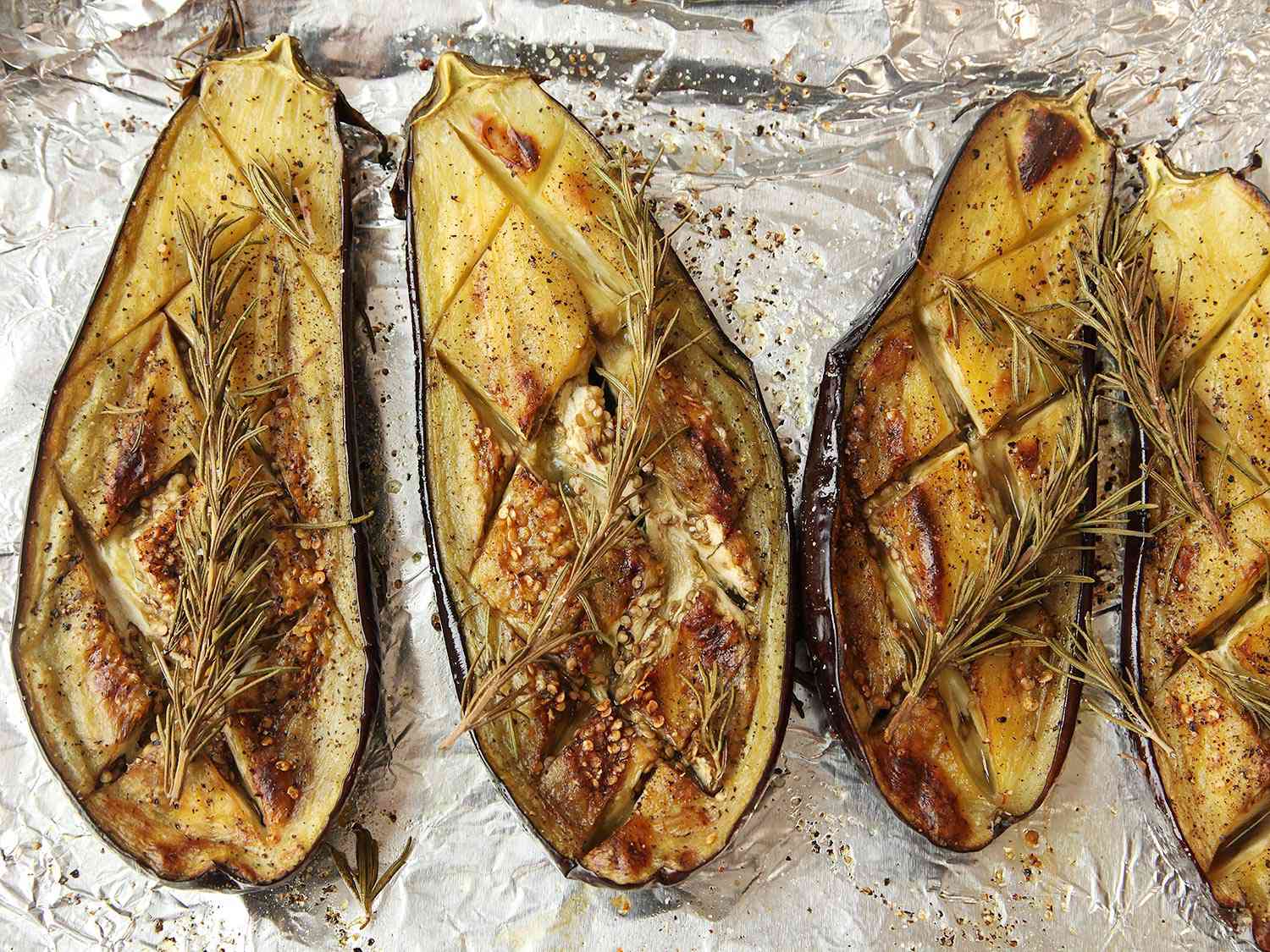 Roasted eggplants with cross-hatch scoring pattern, topped with rosemary sprigs. 