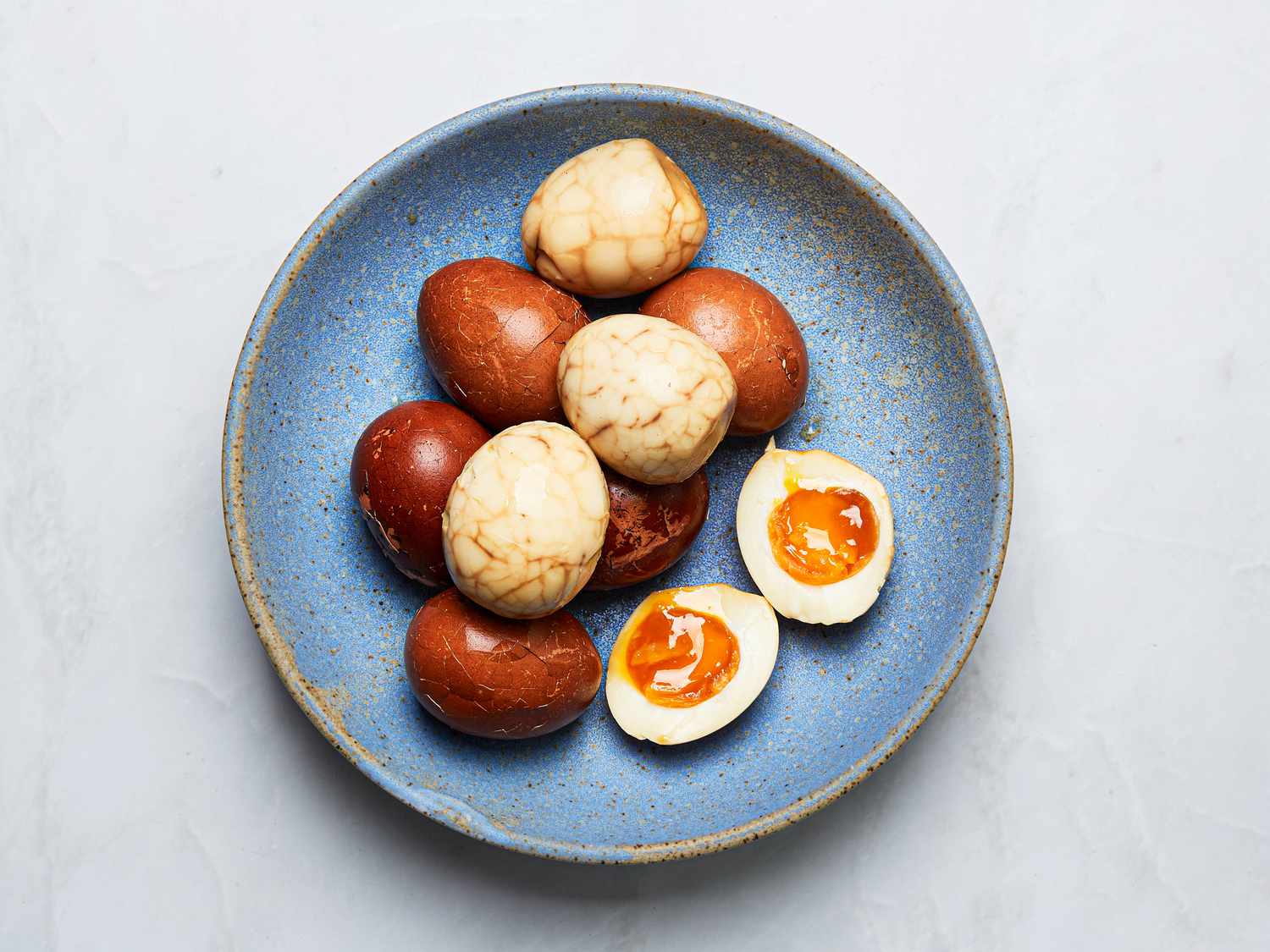 blue bowl of eggs, with some peeled, some with shells on, and one jammy egg sliced in half