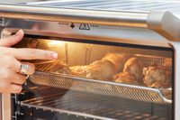 A finger pointing to chicken cooking in the Breville the Smart Oven Air Fryer