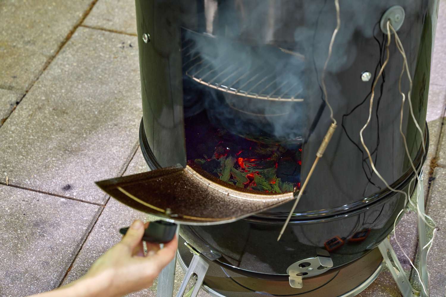 A person opens the door on the base of the Weber 18-Inch Smokey Mountain Cooker