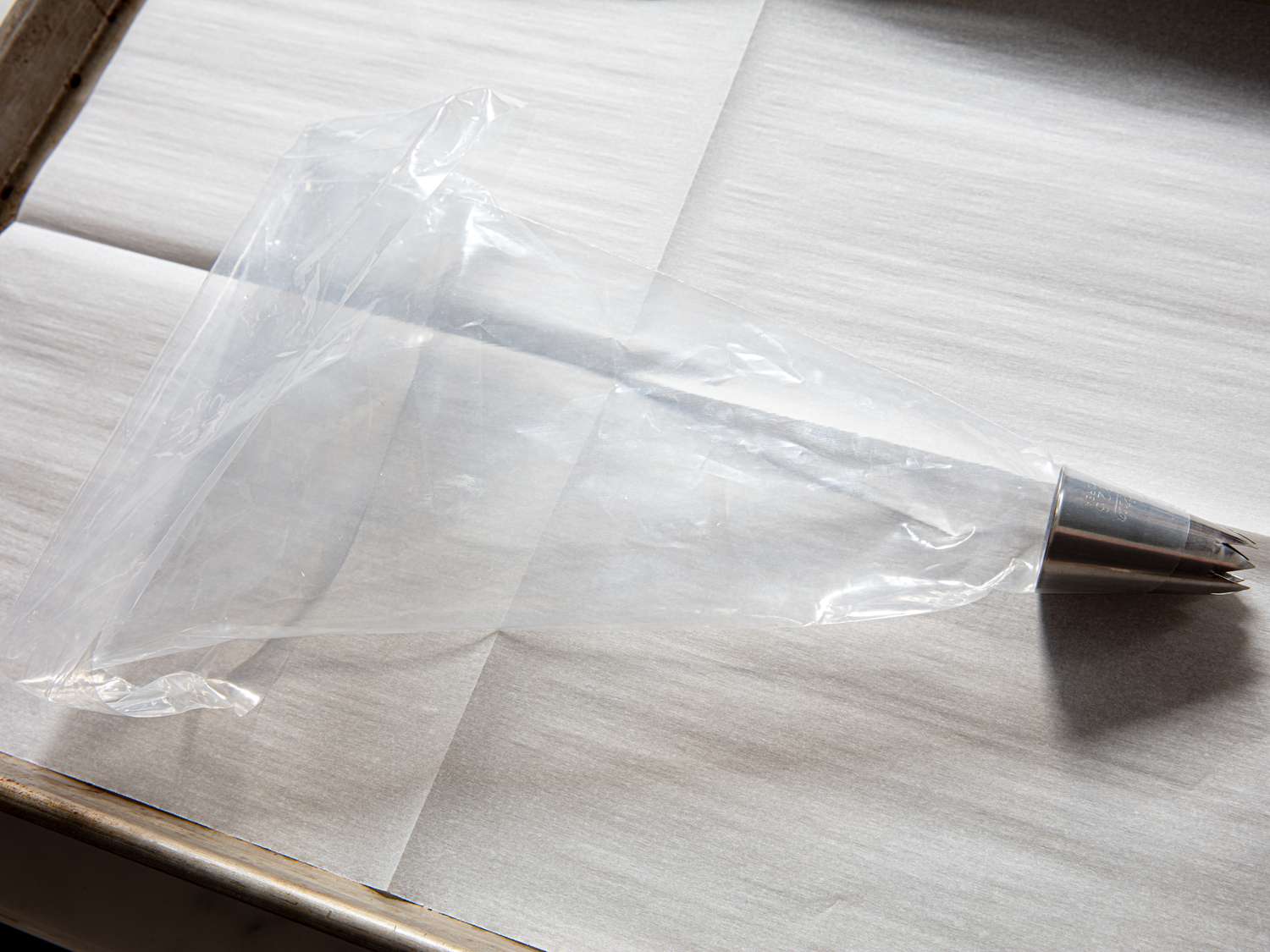 A plastic piping bag with a piping tip on a baking sheet lined with parchment paper.