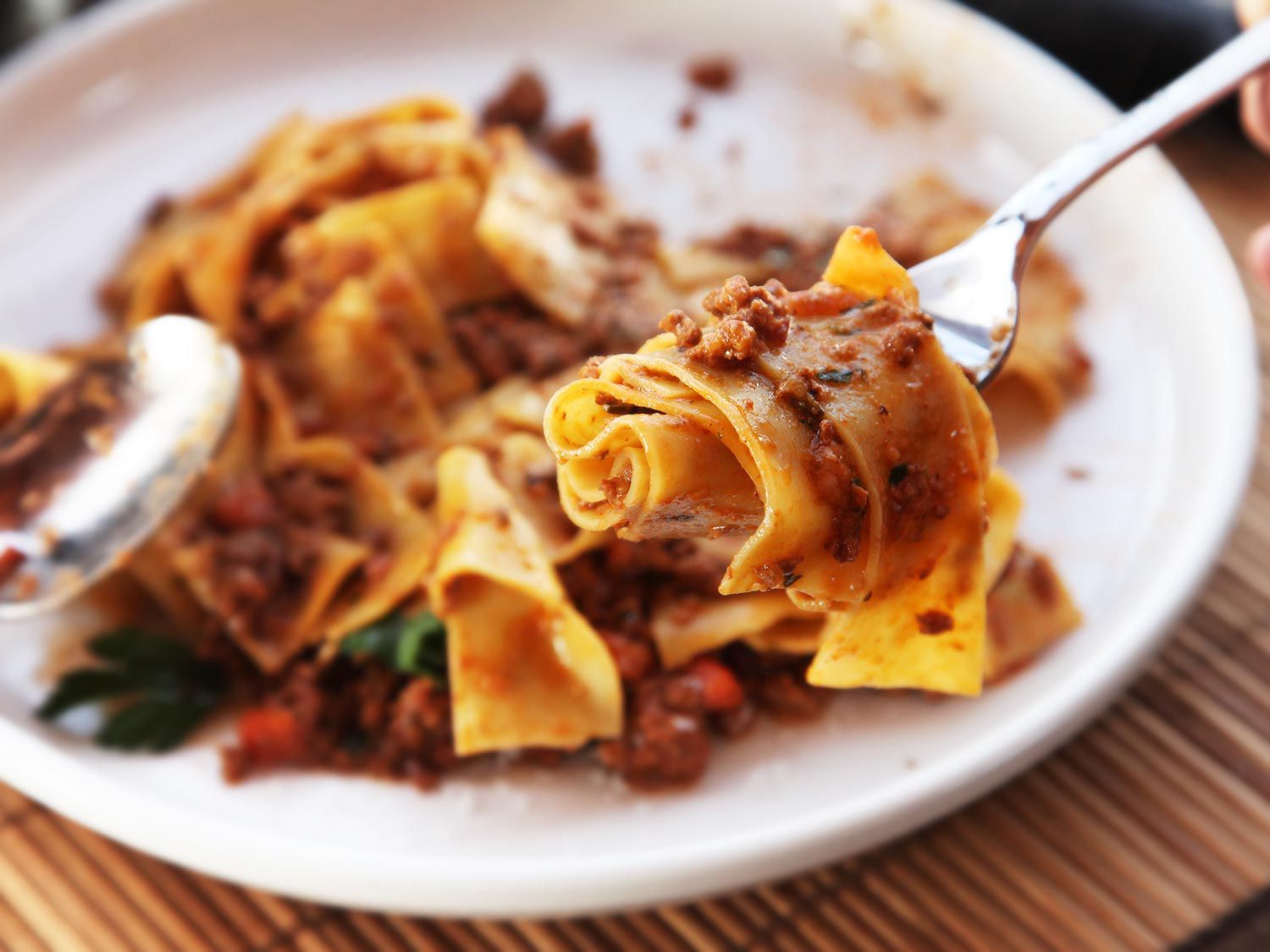 A forkful of Bolognese pasta above a plate containing the rest of the meal.