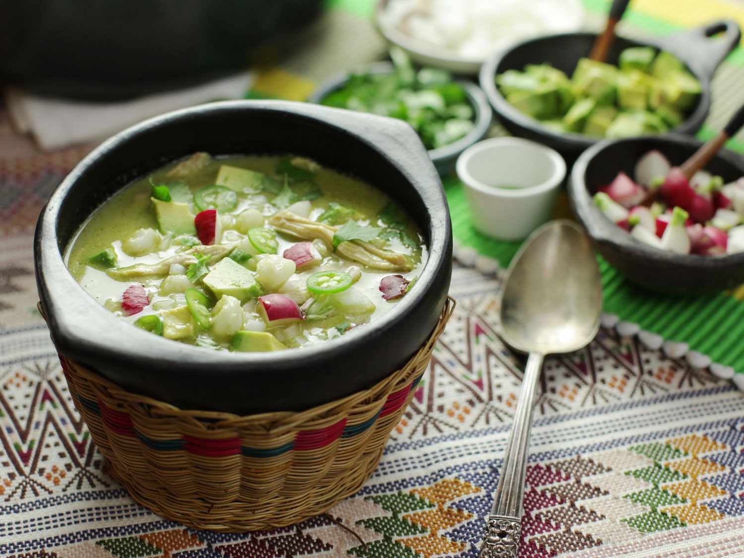 A bowl of green pozole verde topped with avocado and radish.