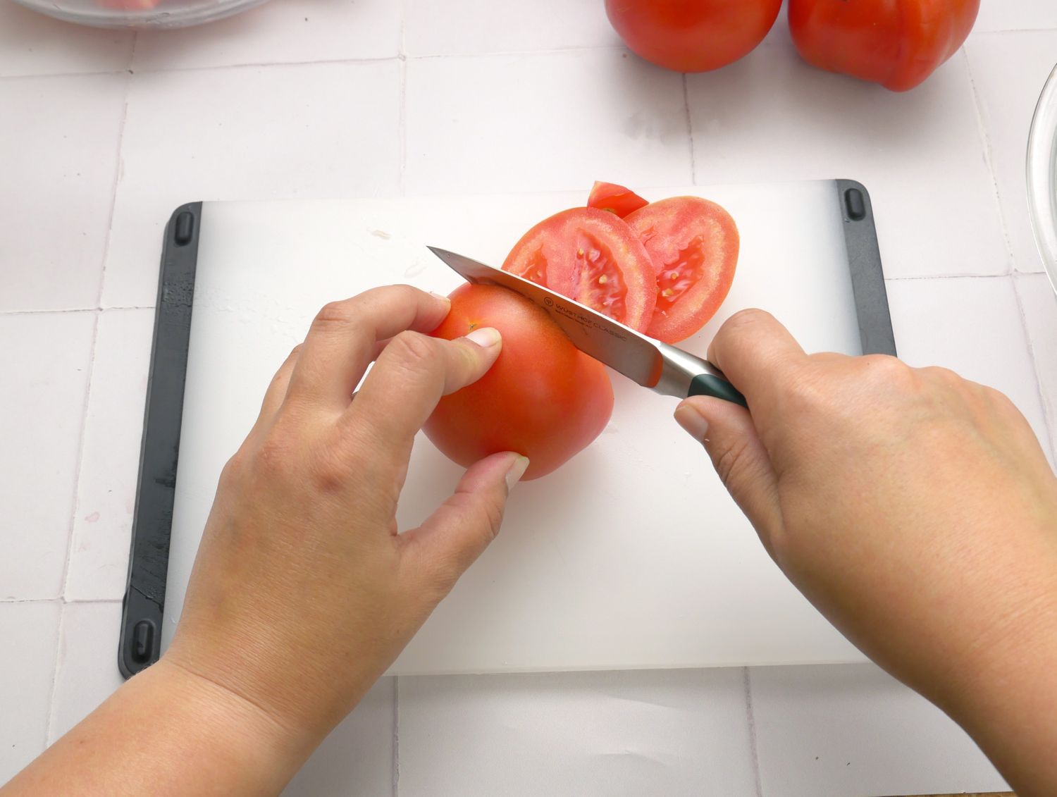 a person slicing a tomato into rounds with a paring knife