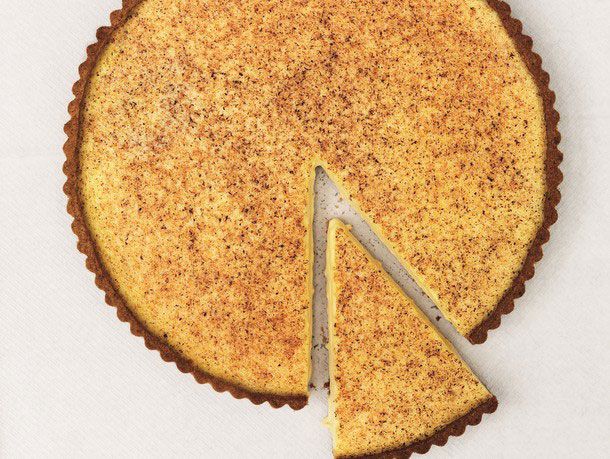 A whole egg custard tart with grated nutmeg. A slice is cut and pulled slightly away. 