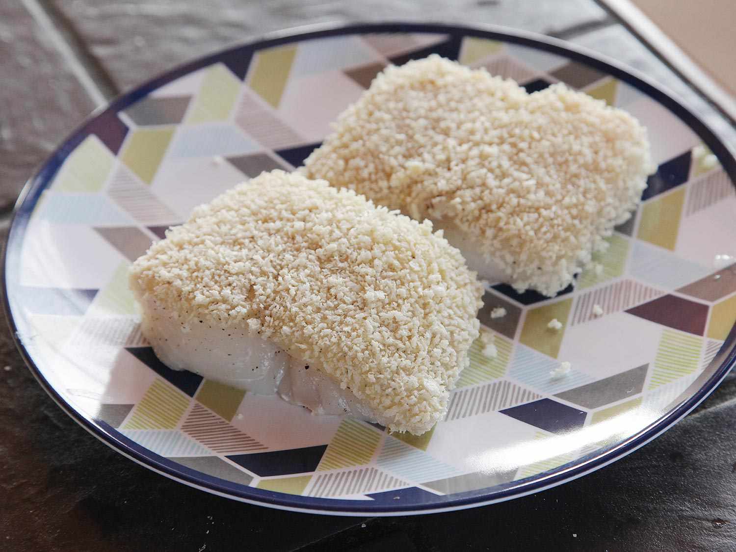 Two fillet portions are transferred to a plate with their floured, egg-dipped, and panko-coated side faced up.