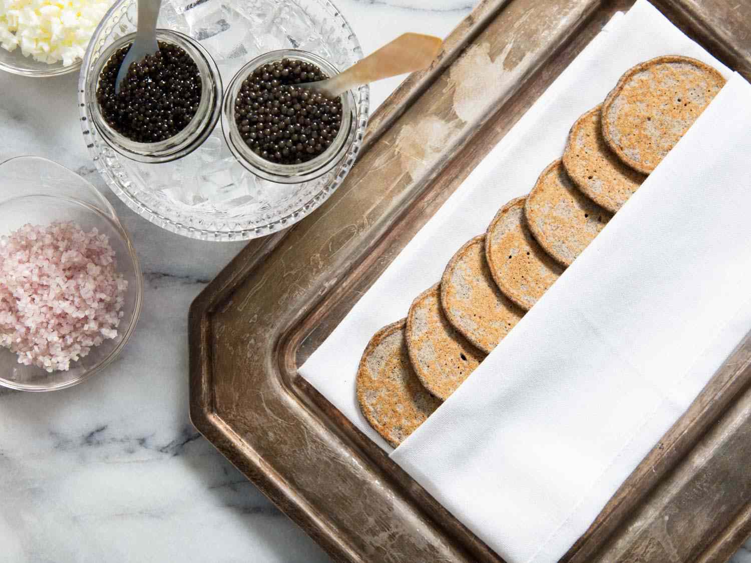 Overhead shot of a platter of buckwheat blini next to 2 small bowls of carviar. 