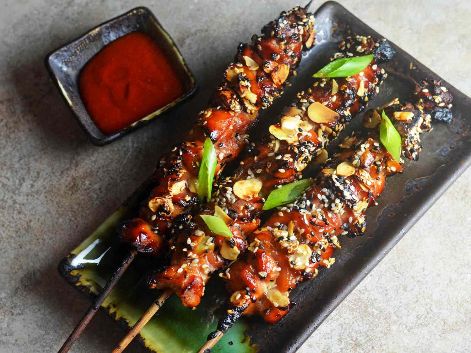 Overhead view of Crispy Caramelized Chicken Skewers, served on a dark green rectangular platter.