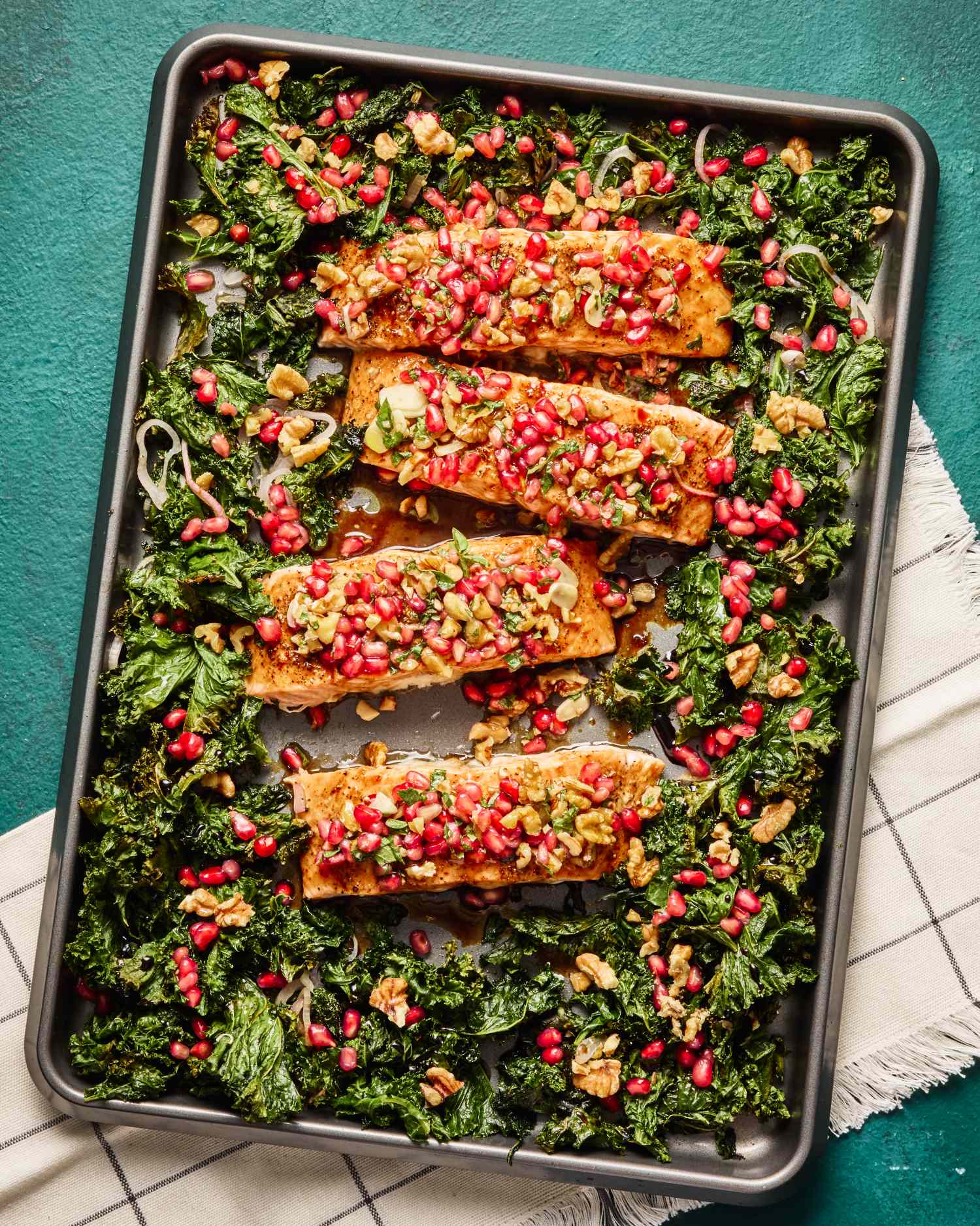 Salmon fillets topped with pomegranate seeds and nuts served on a bed of greens on a tray