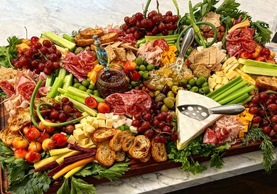 An arrangement of a grazing board adorned with various cheeses meats fruits bread slices and garnishes displayed on a table