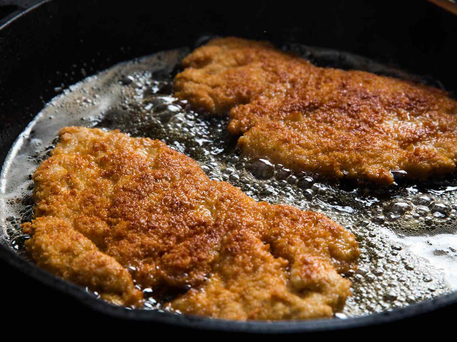 Chicken cutlets pan-frying in a cast iron skillet.