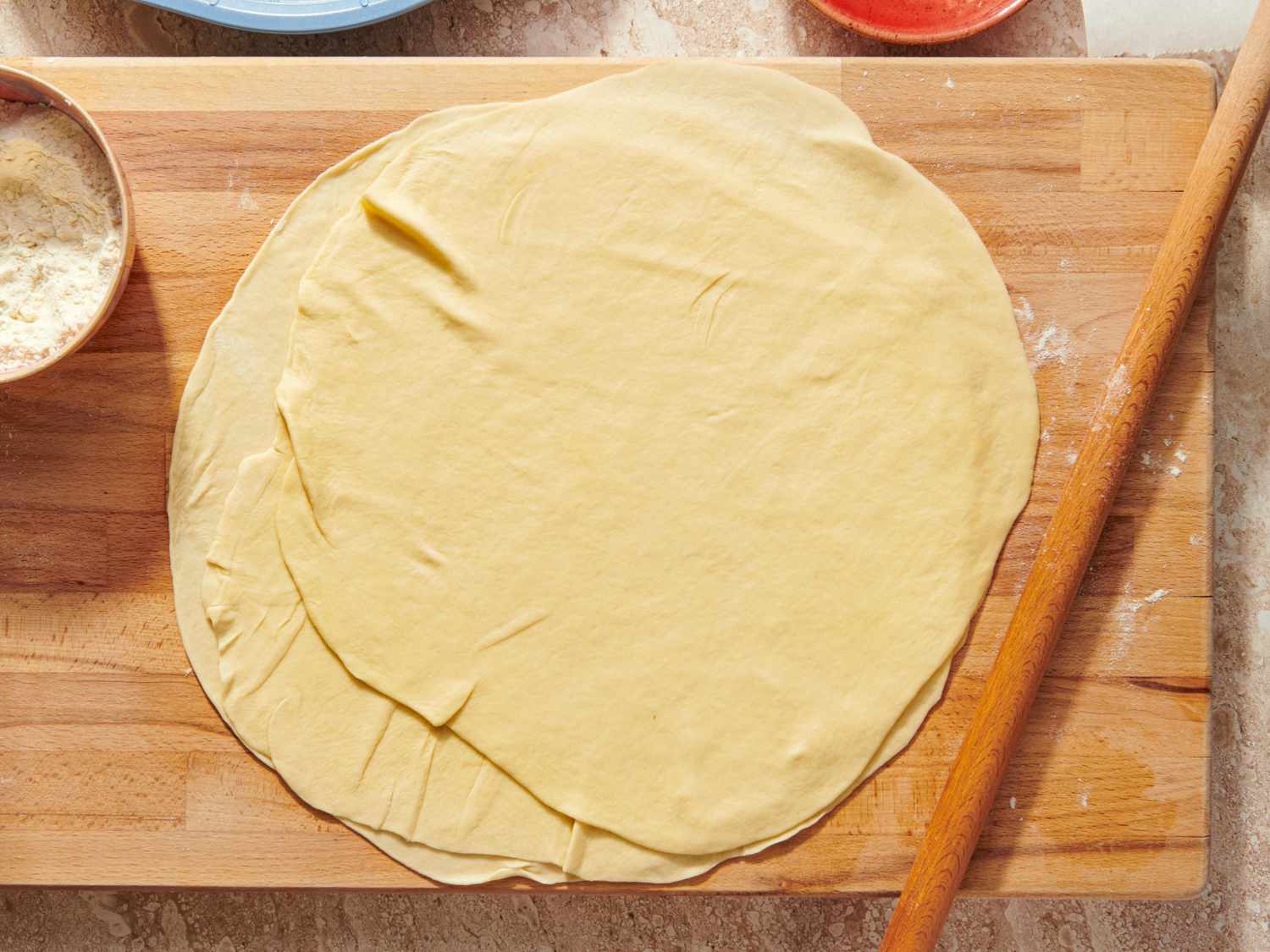 Stack of homemade phyllo dough on a wooden board with a rolling pin