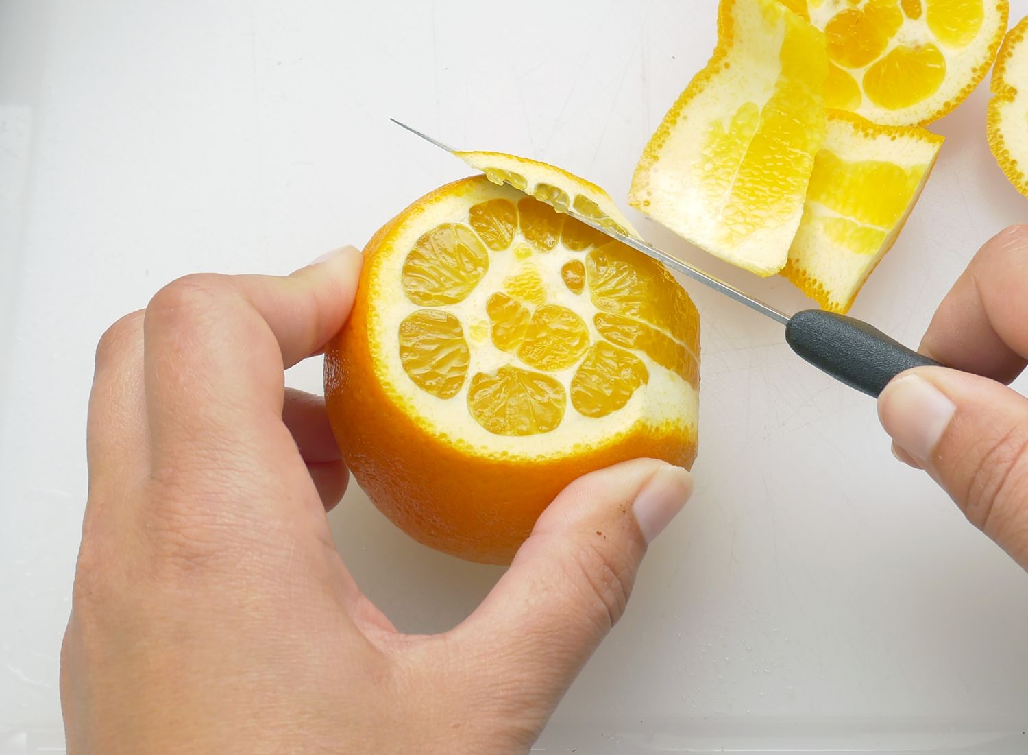 a person slicing off citrus rind 