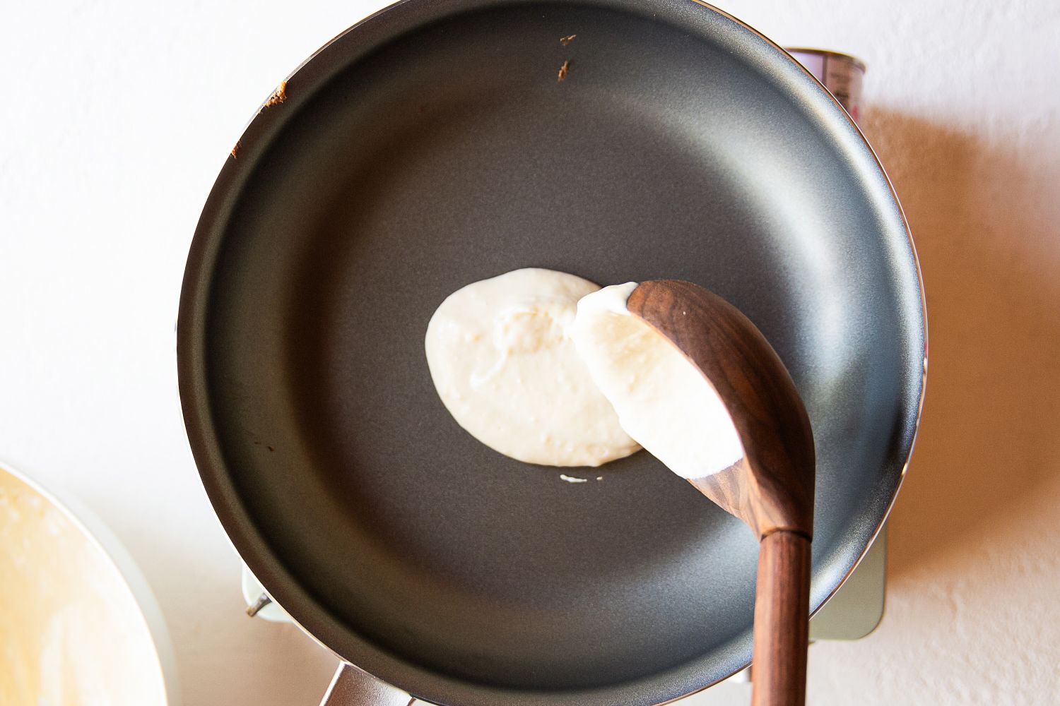 Pancake being spread onto a skillet with a wooden spoon