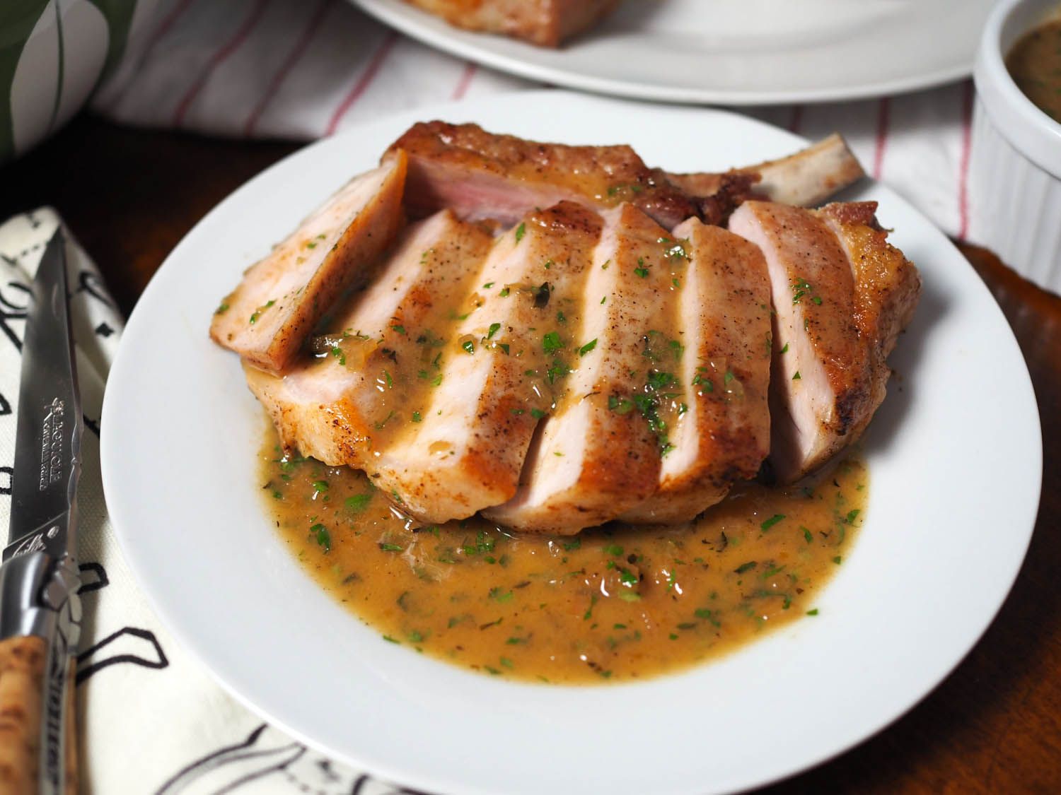 Sliced pork chop on white plate with apple cider pan sauce.