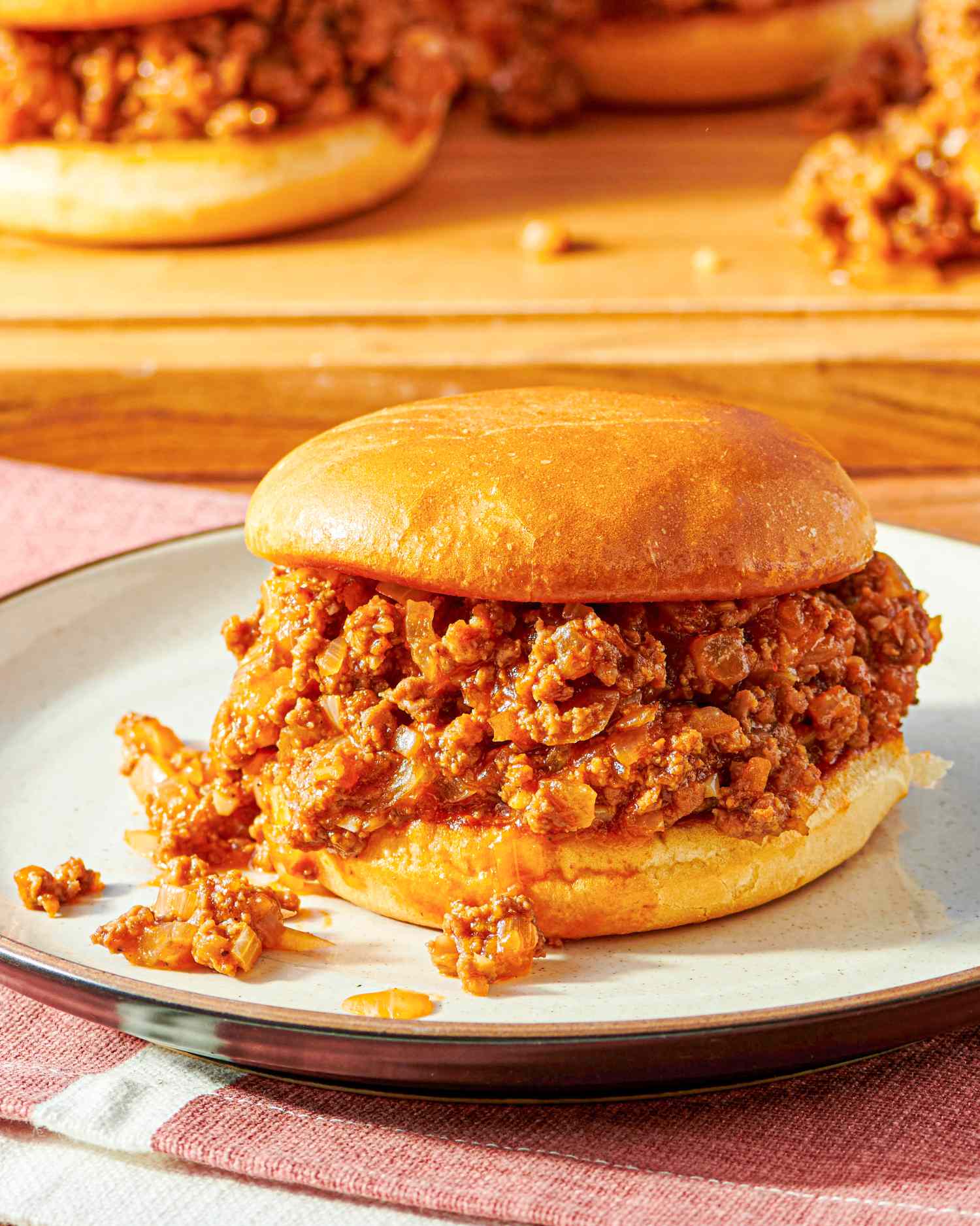 A sloppy joe sandwich on a plate with more sandwiches in the background