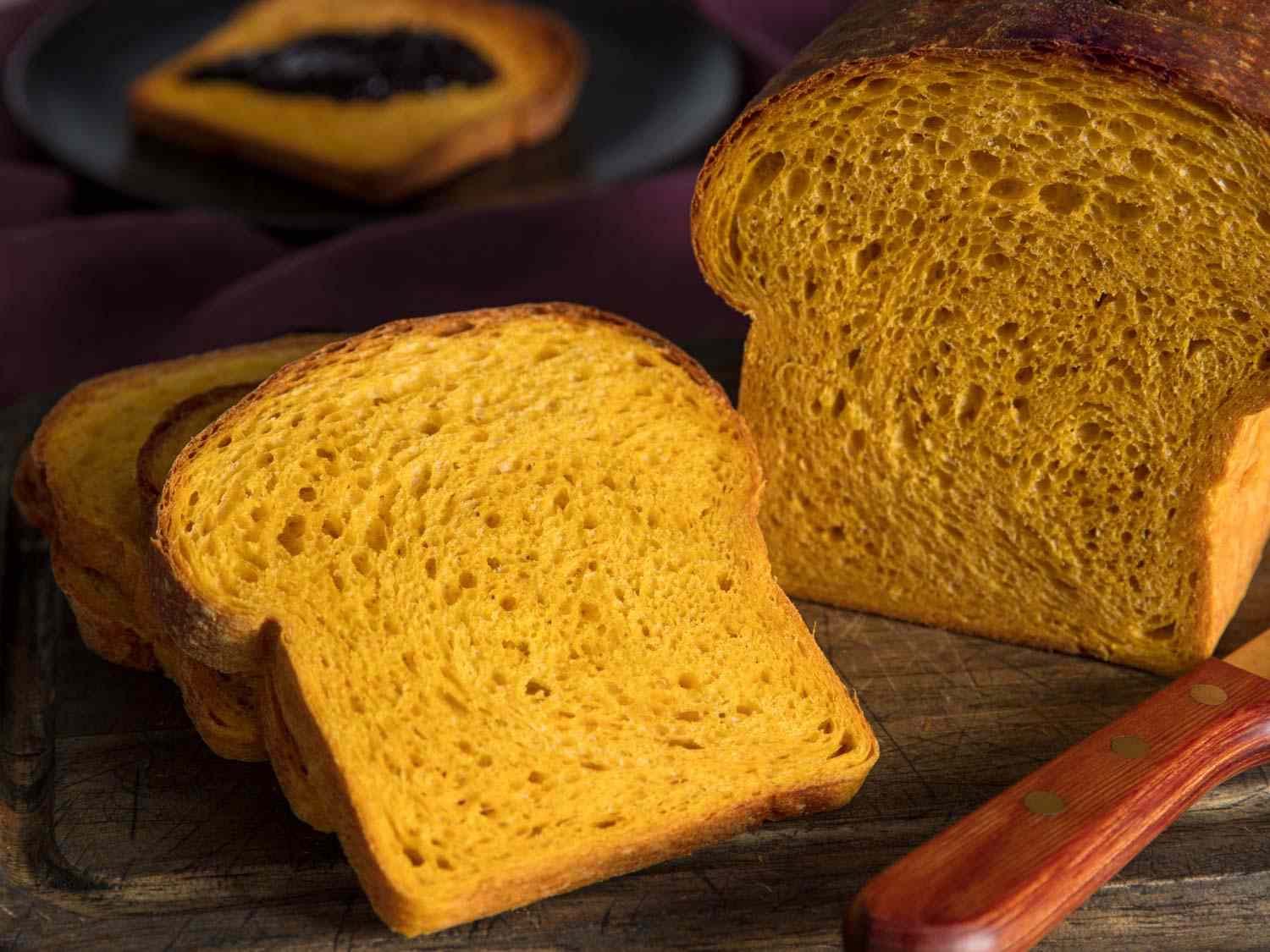 A sliced loaf of pumpkin sandwich bread, with one slice facing up to show the soft interior crumb and pretty orange color.
