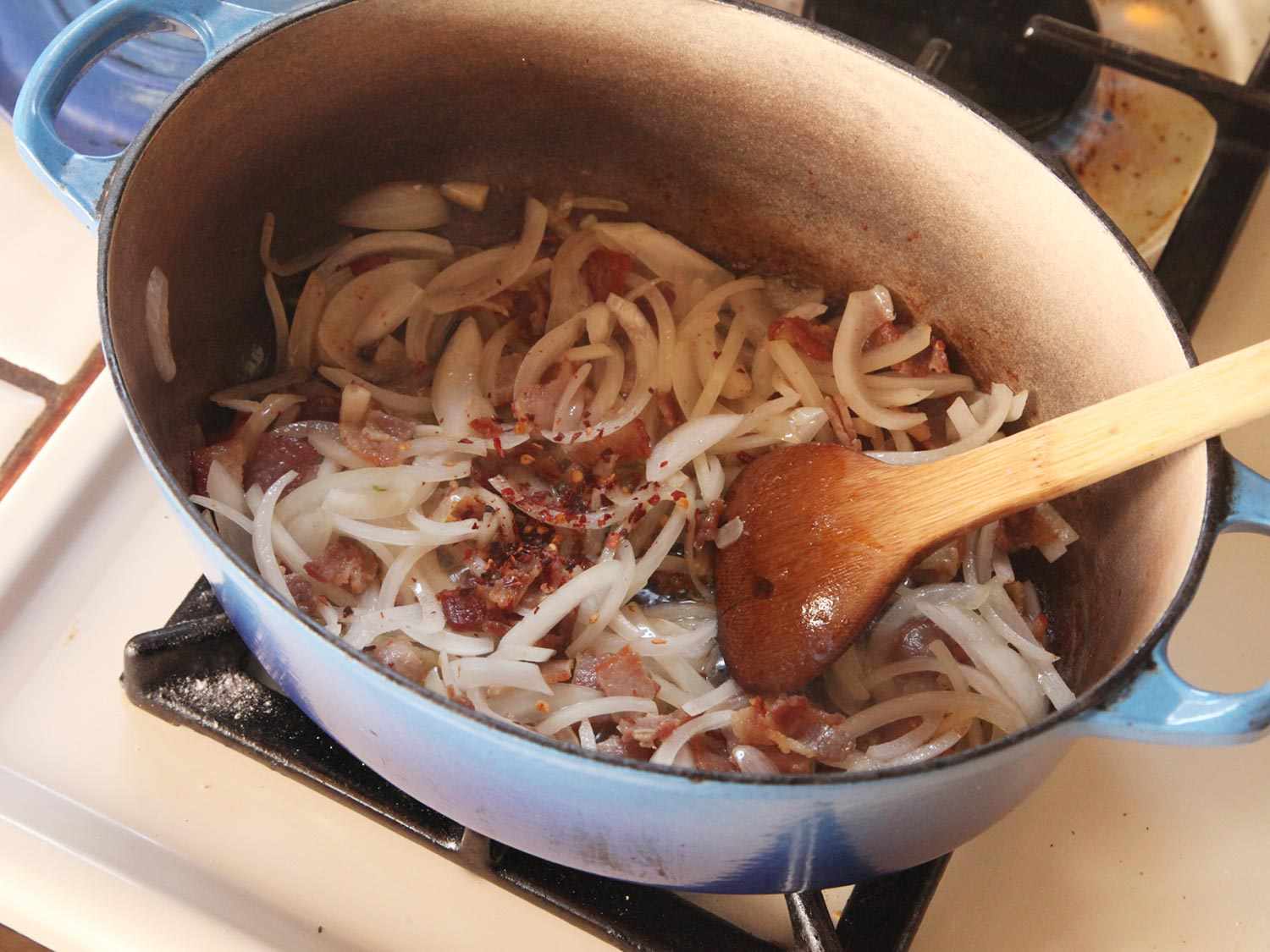 Stirring garlic and red pepper flakes into onions and bacon in Dutch oven