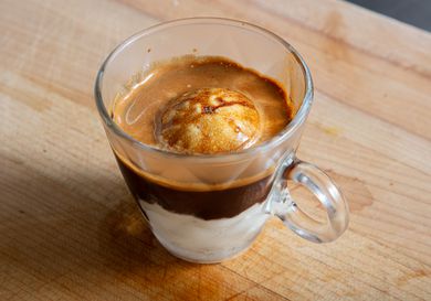 A transparent glass cup containing affogato, an espresso-based dessert with a scoop of vanilla ice cream