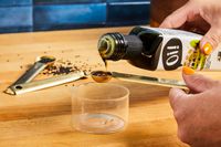 Pouring oil into a measuring spoon with a wooden surface and black sesame seeds in the background