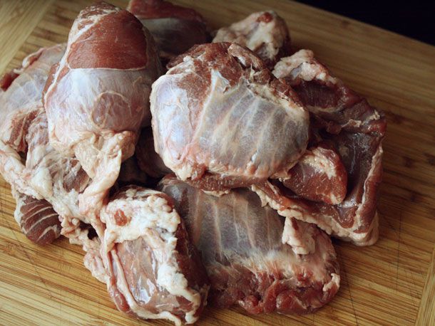 A close-up of untrimmed pork cheeks piled on a bamboo cutting board. 