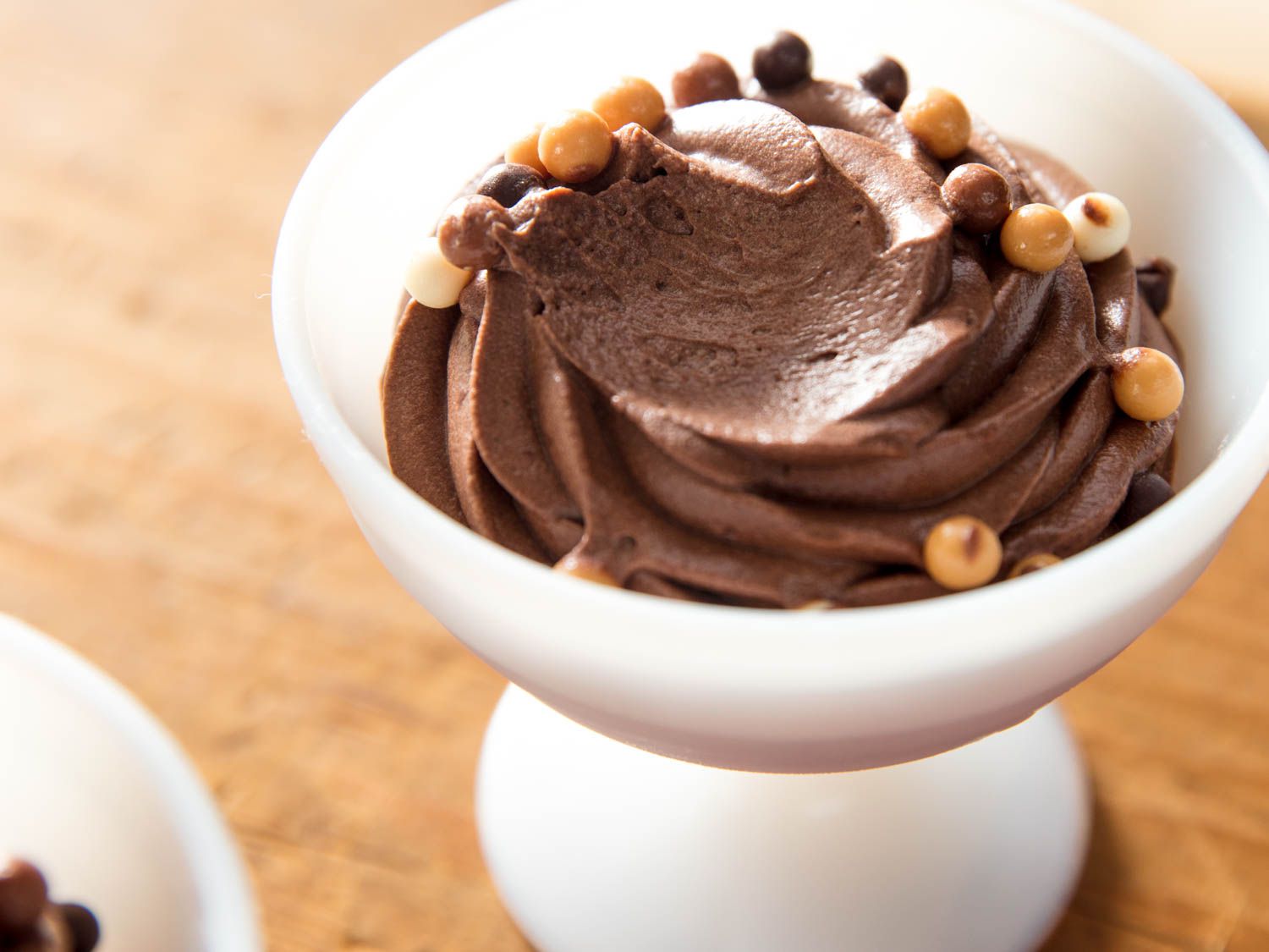 A white dessert bowl filled with eggless chocolate mousse, with one bite missing.