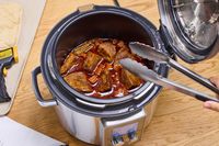 A person stirs cooking meat in the Breville the Fast Slow Pro