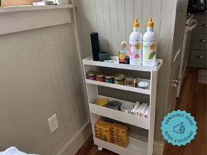 A white kitchen storage rack with olive oil, spices, napkins, and dried goods on its shelves