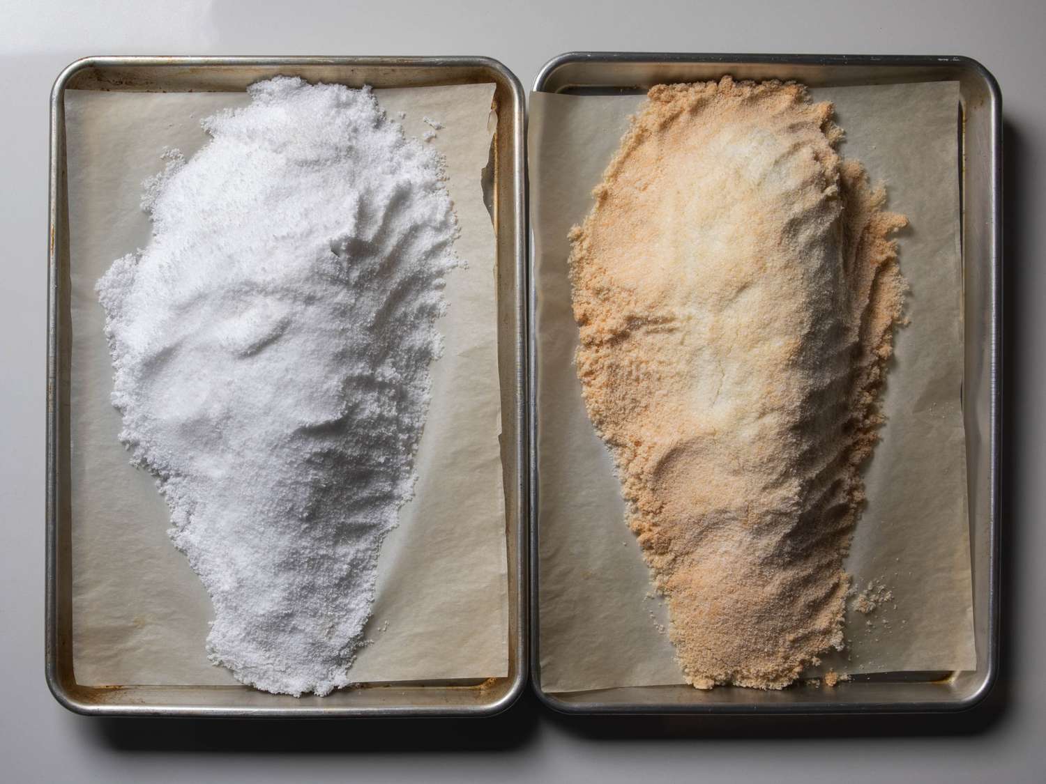 Two side-by-side examples of a salt-baked fish, still in their salt shells. On the left, the salt was mixed only with water, and it remained a plain white color throughout cooking. On the right, the egg-white batch browned during cooking.